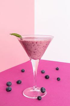 Blueberry smoothie cup with several blueberries on a fuchsia table. Pink and white background.