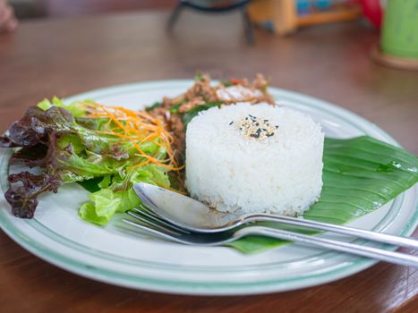 Thai food rice topped with stir fried pork and basil served with vegetables on wooden table. top view.