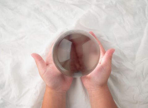 Hand holding a crystal glass ball transparent on white fabric background.