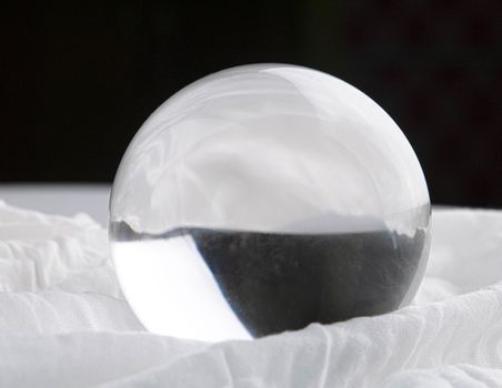 Crystal glass ball sphere transparent on white fabric and dark background.