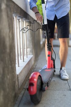 Male user safely parking electric scooter and locking it to a fence. Eco friendly green modern urban mobility concept of sharing transportation with electric scooters for rent in Ljubljana, Slovenia.