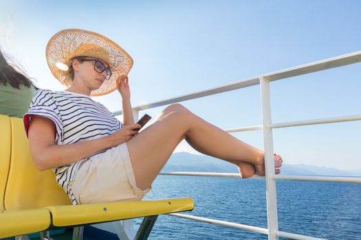 Beautiful, romantic blonde woman on summer vacations traveling by cruse ship ferry boat holding and using mobile phone. Summer vacation lifestyle.