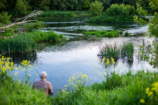 old man fishing with friend on a river at summer daytime with selective focus.