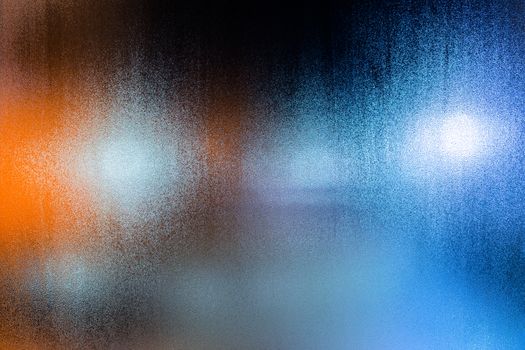 an abstract background of night street lights through wet glass with water drops, close-up with selective focus.