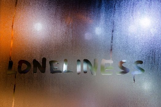the word lonelines written by finger on night wet glass with blurred lights in background.