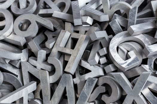 pile of silver metal alphabet characters cutted by waterjet machine - close-up view with selective focus