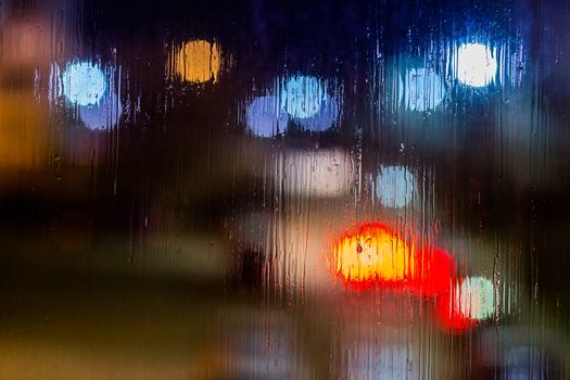 an abstract background night street lights bokeh through wet glass, close-up with selective focus.