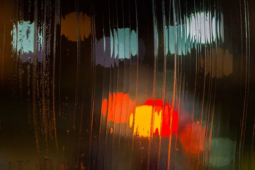 an abstract background night street lights bokeh through wet glass, close-up with selective focus.
