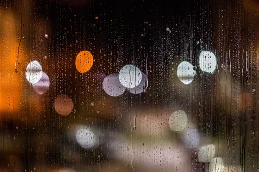 an abstract background night street lights bokeh through wet glass with water smudges, close-up with selective focus.