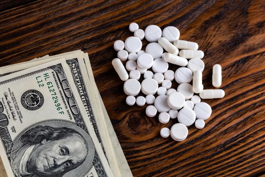 white medicals on brown wood surface near stack of hundred us dollar banknotes
