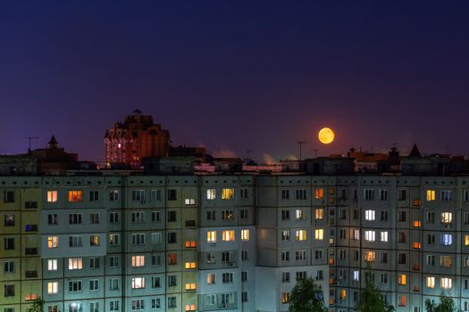 Windows, roofs and facade of an mass apartment buildings in Russia at full moon night. Telephoto closeup shot.