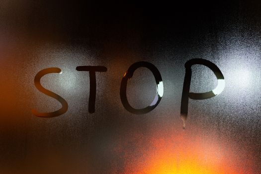 the word stop written on night wet window glass close-up with blurred background.