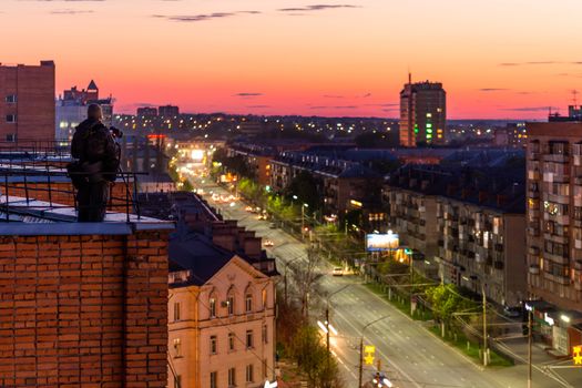 photographer shooting night sity from edge of red brick condominium roof somewhere in eastern europe