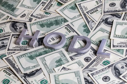 The words HODL laid with aluminium letters on the US dollar banknotes background - with selective focus.