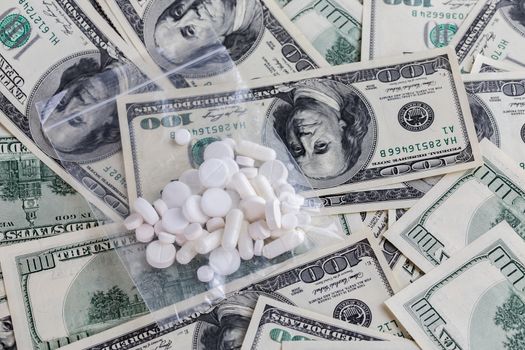 handful of white pills in small transparent plastic bag on dollar bills close-up with selective focus