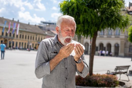 Old man coughs and sneezes into a handkerchief on street, outdoor, hot summer, allergies and illness concept