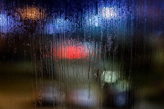 an abstract background night street lights bokeh through wet glass, close-up with selective focus.