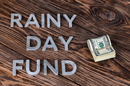 the words RAINY DAY FUND laid by metal letters near small pack of us dollars on wooden background
