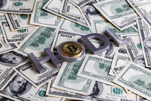 The words HODL laid with aluminium letters and bitcoin shiner on the US dollar banknotes background - with selective focus and diagonal composition.