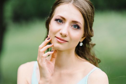 Happy girl in a turquoise long dress in a green park on a background of herbs, trees and rose bushes