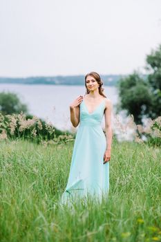 Happy girl in a turquoise long dress in a green park on a background of herbs, trees and rose bushes