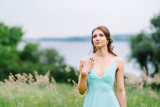 Happy girl in a turquoise long dress in a green park on a background of herbs, trees and rose bushes