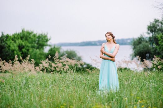 Happy girl in a turquoise long dress in a green park on a background of herbs, trees and rose bushes