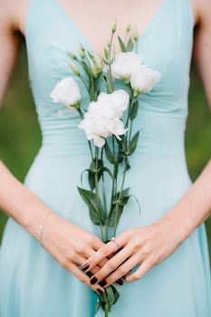 Happy girl in a turquoise long dress in a green park on a background of herbs, trees and rose bushes