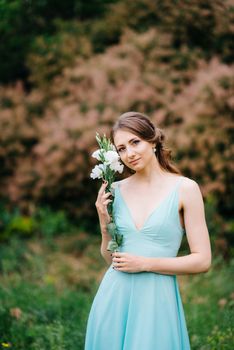 Happy girl in a turquoise long dress in a green park on a background of herbs, trees and rose bushes