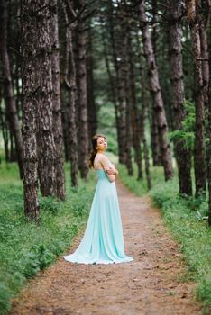 Happy girl in a turquoise long dress in a green park on a background of herbs, trees and rose bushes