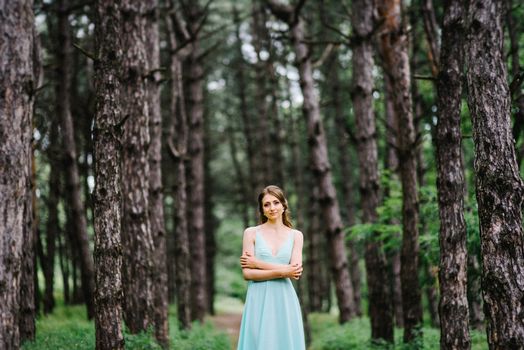 Happy girl in a turquoise long dress in a green park on a background of herbs, trees and rose bushes