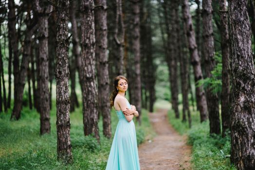 Happy girl in a turquoise long dress in a green park on a background of herbs, trees and rose bushes