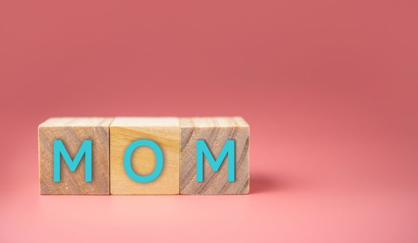 MOM Word Written In Wooden Cube on pink background. Mother's day concept.