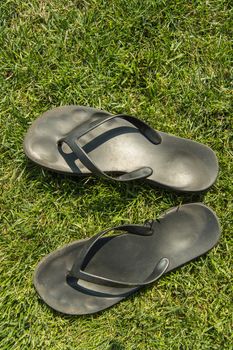 A pair of black rubber flip-flops on the green lawn grass with a copy of the space, summer, outdoor, top view, vertical frame.