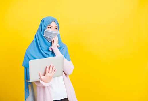 Asian Muslim Arab, Portrait of happy beautiful young woman Islam religious wear veil hijab and face mask protect she quarantines disease coronavirus hold laptop computer and thinking question