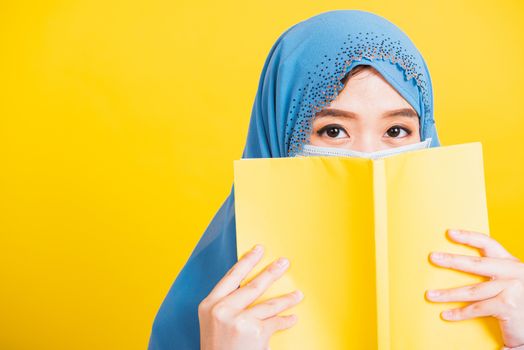 Asian Muslim Arab, Happy beautiful young woman religious wear veil hijab and face mask to prevent coronavirus she student hold books close face, isolated on yellow background, Back to college