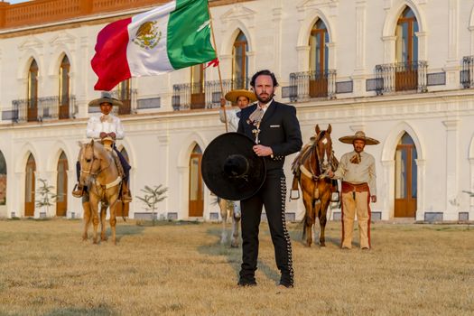 A handsome Mexican Charro poses in front of a hacienda in the Mexican countryside