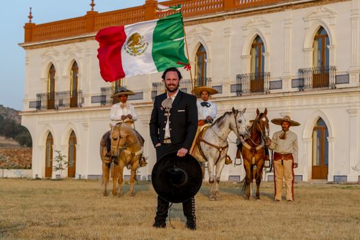 A handsome Mexican Charro poses in front of a hacienda in the Mexican countryside