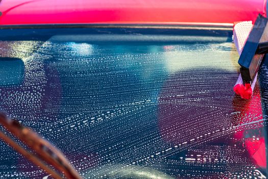 Washing and cleaning the front window of a car with mop in self service car wash station, close up isolated.