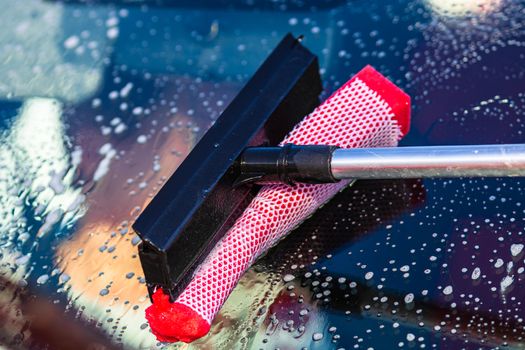 Washing and cleaning the front window of a car with mop in self service car wash station, close up isolated.