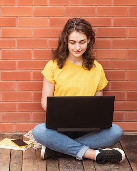 young woman in yellow shirt sitting on flor, holding and working on the laptop