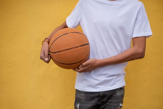 Basketball in hand of young person against yellow background