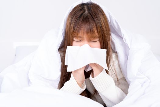Asian woman blowing a nose to tissue lying on the bed at home. Healthcare medical or daily life concept.
