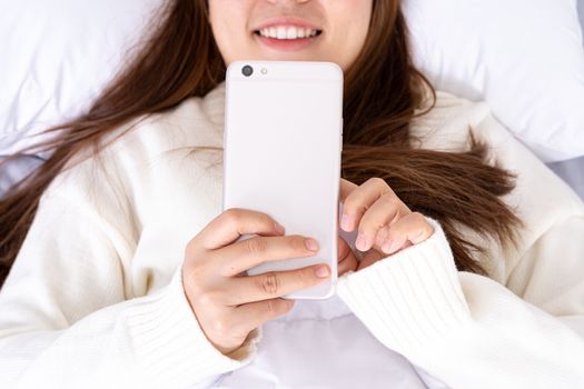 Happy Asian girl using a mobile phone lying on the bed at home. Social and technology concept.