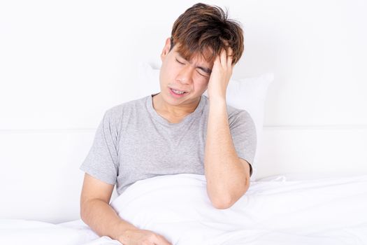 Young man suffering from headaches after wake up on the bed. Healthcare medical or daily life concept.