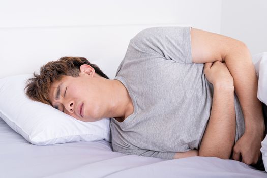 Young man suffering stomach aches lying on the bed. Healthcare medical or daily life concept.