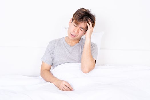 Young man suffering from headaches after wake up on the bed. Healthcare medical or daily life concept.