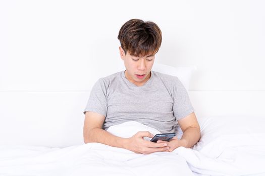 Happy Asian man using a mobile phone lying on the bed at home. Social and technology concept.