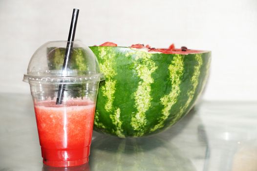 fresh watermelon in a glass with a straw and half a watermelon.