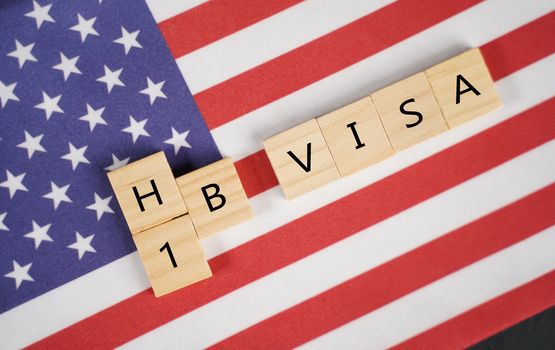 Concept of H1b Visa for foreign workers showing wooden letters with US or United states flag as background.